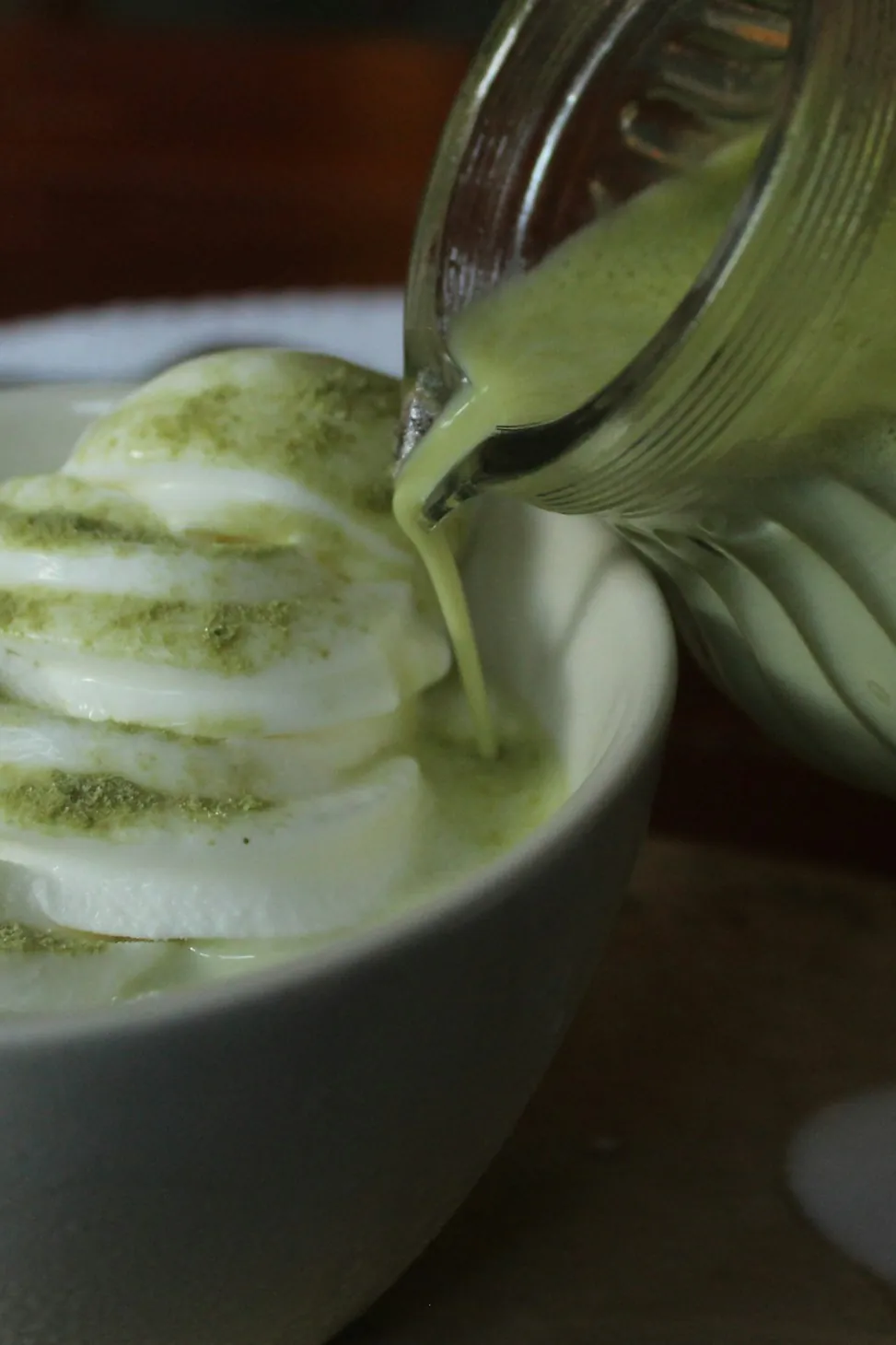 Matcha vertido desde una jarra de vidrio sobre helado de vainilla en un tazón