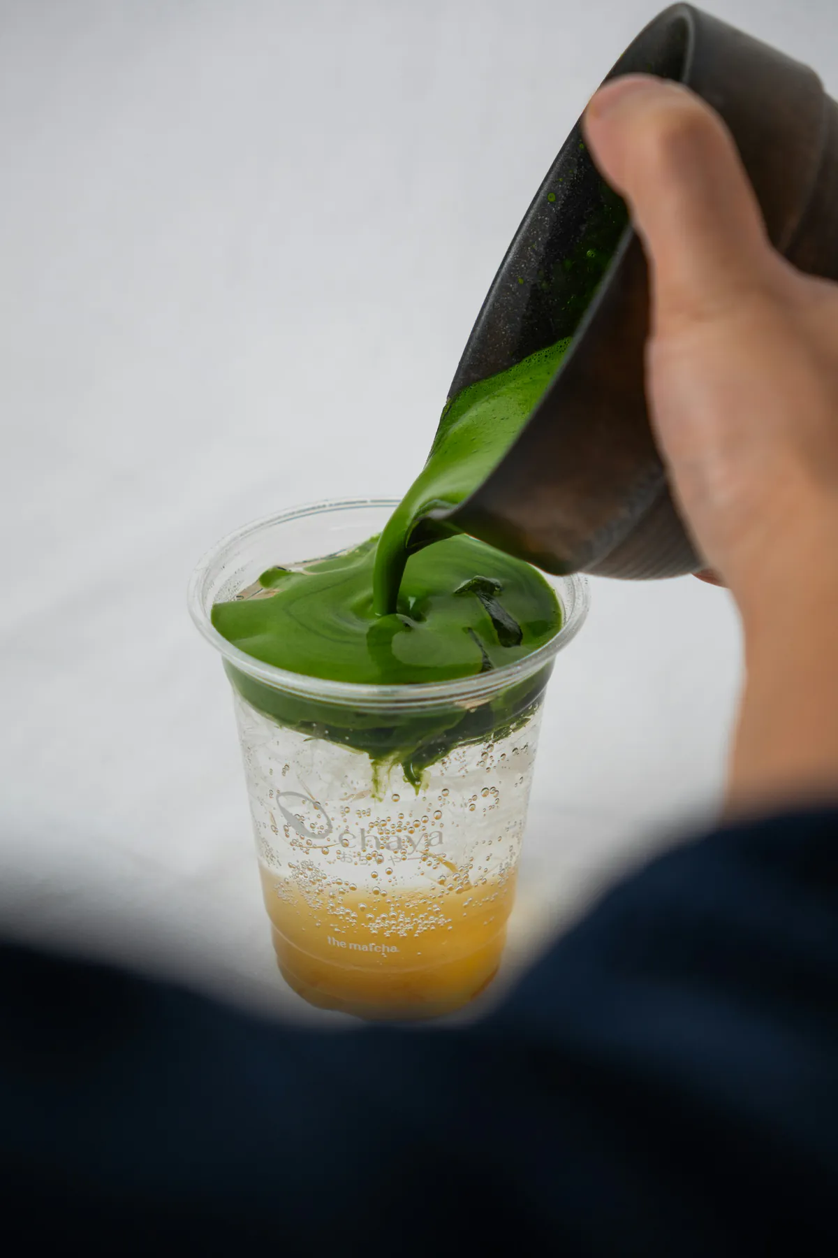 Matcha vertido sobre una bebida cítrica con hielo en un vaso transparente