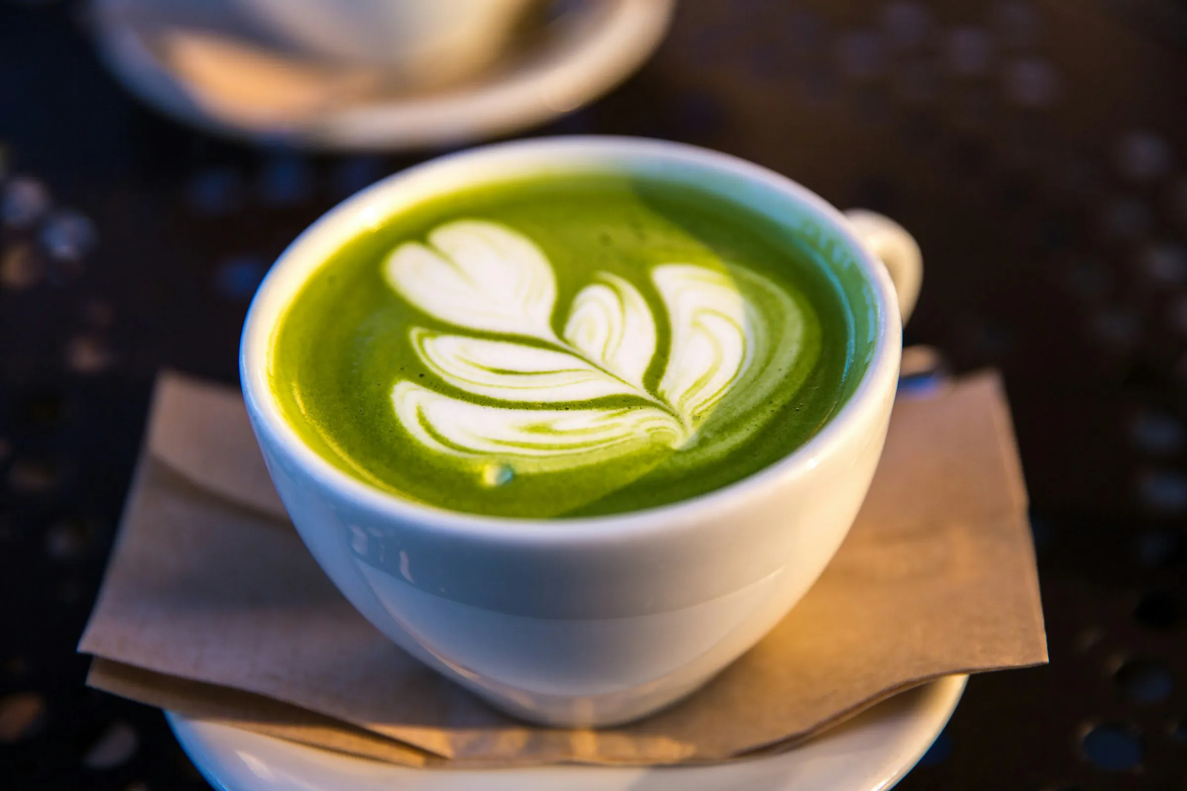 Matcha latte con arte latte en una taza blanca de cerámica, con luz cálida