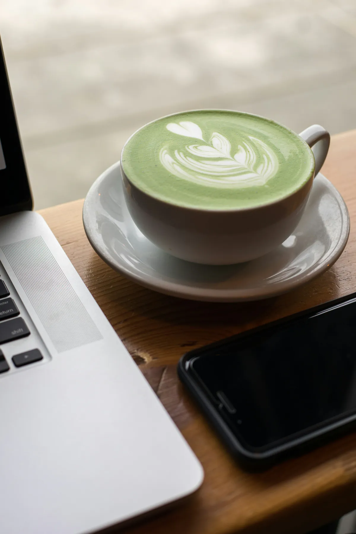 Un matcha latte junto a una laptop y un celular sobre una mesa de madera: una pausa en medio del trabajo