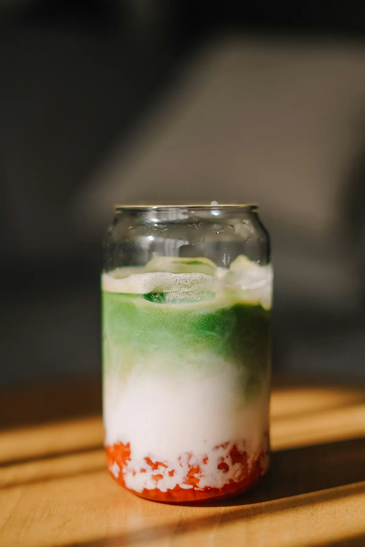 Strawberry matcha en un vaso de vidrio con tres capas: fresa, leche y matcha, bajo la luz del sol