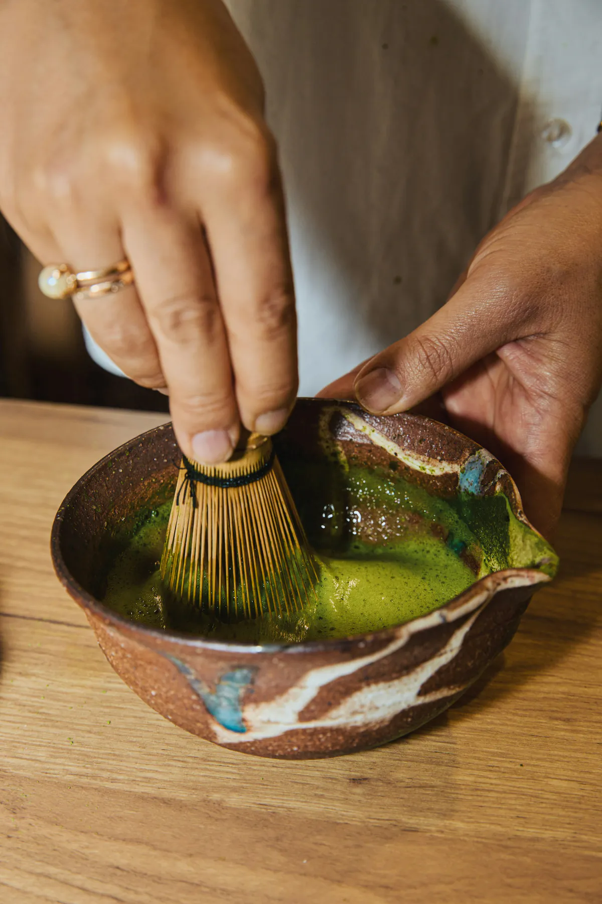 Manos batiendo matcha con un batidor de bambú en un tazón de cerámica artesanal